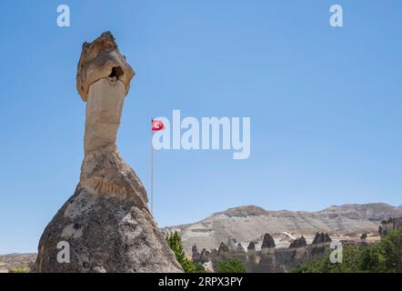 Ein großer Feenschornstein im Freilichtmuseum von Goreme in Kappadokien, Anatolien Türkei, mit einer türkischen Flagge, die horizontal im Wind winkt Stockfoto