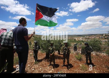 200529 -- SALFIT, 29. Mai 2020 Xinhua -- Ein Palästinenser hält eine palästinensische Flagge vor israelischen Soldaten während eines Protestes gegen israelische Siedlungen und die israelischen Annexierungspläne im palästinensischen Dorf Haris in der Nähe der Westbank-Stadt Salfit, 29. Mai 2020. Die Annexion ist in der Tat Teil des Friedensplans des US-Präsidenten Donald Trump für den Nahen Osten, besser bekannt als das Abkommen des Jahrhunderts. Der Plan wird von den Palästinensern und der arabischen Welt sowie von internationalen Organisationen wie der UNO, die den Plan als Verstoß gegen das Völkerrecht anprangerten, entschieden abgelehnt. Foto von A Stockfoto