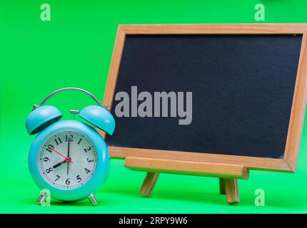 Tafel mit Wecker auf grünem Hintergrund. „Back to School“-Konzept. Stockfoto