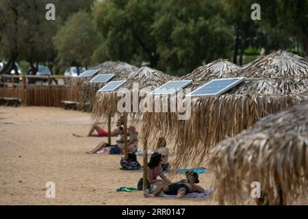 200721 -- ATHEN, 21. Juli 2020 Xinhua -- Foto aufgenommen am 21. Juli 2020 zeigt Sonnenkollektoren auf Sonnenschirmen an einem offenen öffentlichen Strand in der Nähe des Rathauses der Gemeinde Vari-Voula-Vouliagmeni im Süden Athens, Griechenland. Ab Dienstag sind die Dutzenden Sonnenschirme, die entlang des Strandes verstreut sind, im Einklang mit den Maßnahmen zur sicheren Entfernung zum Schutz vor COVID-19 mit einem System ausgestattet, das aus Solarpaneelen und USB-Anschlüssen besteht, die kostenlose und umweltfreundliche Ladungen ermöglichen. Im Rahmen eines Pilotprogramms, das am Dienstag gestartet wurde, werden Sonnenanbeter mit Solarenergie zu Energieeinsparungen beitragen Stockfoto