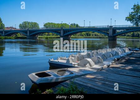 Freizeitboote und Tretschuhe legen am Dock und Becken des Tormes River an, während die Enrique Esteban Iron Bridge bei Sonnenuntergang im Hintergrund liegt. Stockfoto