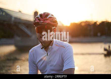 Der Mann trägt einen Schutzhelm, eine Sonnenbrille und Sportkleidung während der abendlichen Fahrt in der Stadt. Nahaufnahme Stockfoto