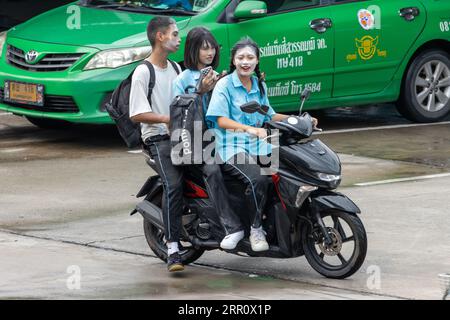 SAMUT PRAKAN, THAILAND, Juni 06 2023, Ein Trio von Teenagern mit Puder auf ihren Gesichtern, die mit einem Motorrad im Regen fahren Stockfoto