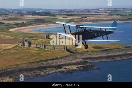 Die Tiger Moth aus dem Zweiten Weltkrieg führt über Dunstanburgh Castle in Northumberland in den Himmel. Die DH82A Tiger Moth wurde 1940 gebaut und gehört Darren Davis und Dave Burns von Tiger Flights, einem unabhängigen Unternehmen mit Sitz auf dem Eshott Airfield. Je nach Wetterlage wird G-EMSY das ganze Jahr über fliegen, was Luftfahrtfans das unvergleichliche Erlebnis des Cockpitflugs mit offenem Cockpit und einen einzigartigen Blick auf die Landschaft von Northumberland und ikonische Wahrzeichen bietet. Bilddatum: Dienstag, 5. September 2023. Stockfoto