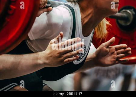 Weibliche Powerlifter beim Hocken des Powerlifters sind die Hände des Trainers auf dem Sicherheitsnetz Stockfoto