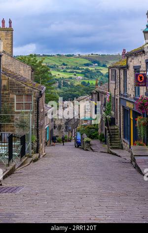 Das hübsche Dorf Haworth, in der Nähe von Keighley in den Pennines, West Yorkshire. Diese legendäre steile Straße ist die Main Street, gesäumt von schönen Cottages. Stockfoto