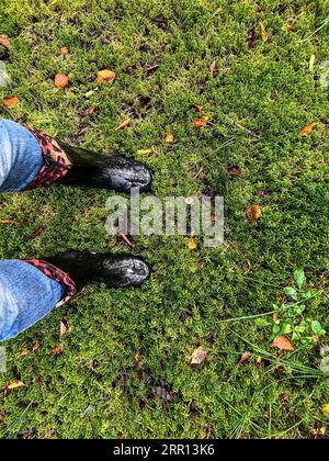 Die Beine der Frau tragen schwarze Wellingtons auf grünem Grasgrund. Hochwertige Fotos Stockfoto