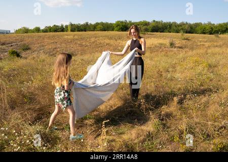 Mutter und Tochter bereiten sich auf ein Picknick auf dem Sommerfeld vor und legen eine Decke auf das Gras Stockfoto
