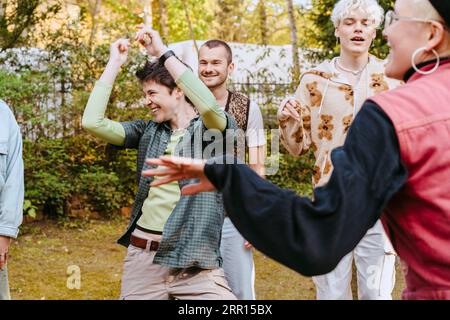 Glückliche nicht-binäre Person tanzt unter LGBTQ-Freunden während der Party im Hinterhof Stockfoto