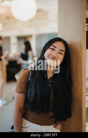 Porträt einer lächelnden jungen Studentin, die sich an die Wand lehnt Stockfoto