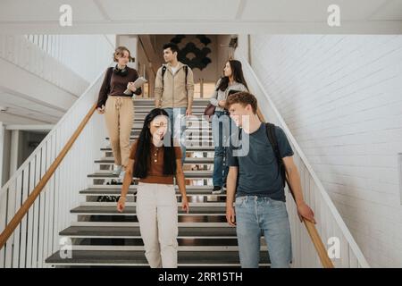 Glückliche multirassische männliche und weibliche Studenten, die auf Stufen in der Universität gehen Stockfoto