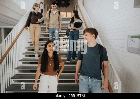 Glückliche multirassische Studenten sprechen, während sie auf Stufen in der Universität gehen Stockfoto