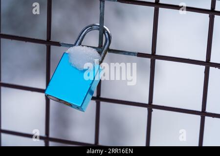 Blaues Liebesschloss mit Schnee auf einem Metallzaun im Winter mit unscharfem Hintergrund, Modell. Stockfoto