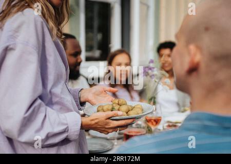 Der Mittelteil einer Frau, die Babykartoffeln auf Tellern hält, während der Dinnerparty im Café Stockfoto