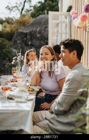 Lächelnder junger Mann, der mit männlichen Freunden sitzt und eine Dinnerparty im Café feiert Stockfoto
