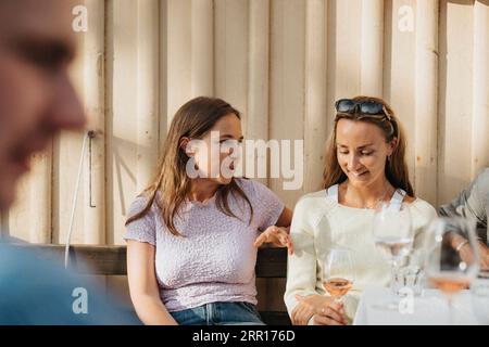 Junge Frau, die mit einer Freundin während einer Dinnerparty im Café spricht Stockfoto