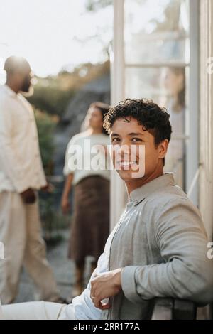 Seitenansicht des lächelnden jungen Mannes während der Dinnerparty im Café Stockfoto