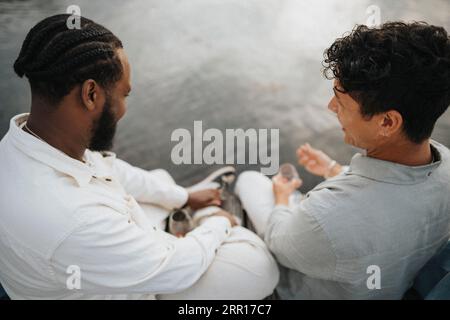 Blick auf junge männliche Freunde, während sie in der Nähe des Sees sitzen Stockfoto