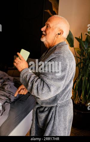 Seitenansicht des Seniorenmenschen, der zu Hause im Schlafzimmer tanzt und Musik hört Stockfoto
