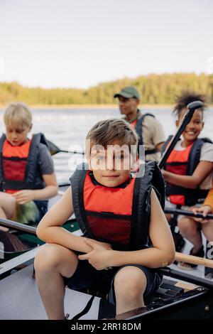 Porträt eines Jungen, der eine Schwimmweste trägt, während er im Kajak im Sommercamp sitzt Stockfoto