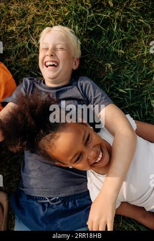 Direkt über dem Schuss fröhlicher männlicher und weiblicher Freunde, die beim Sommercamp auf Gras liegen Stockfoto