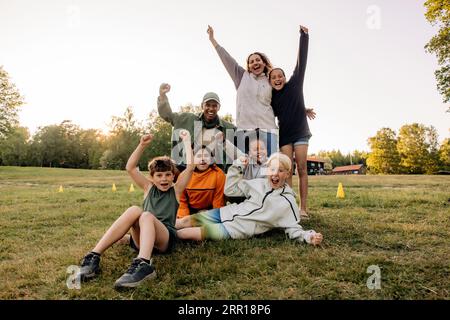 Porträt fröhlicher Kinder, die mit Ratgebern auf dem Rasen auf dem Spielplatz im Sommercamp schreien Stockfoto