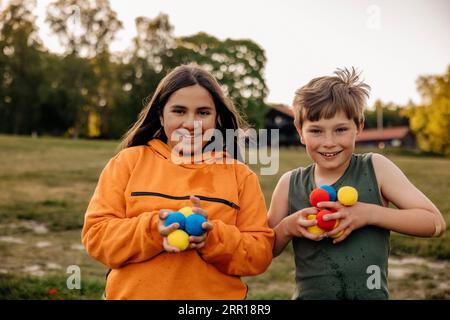 Porträt glücklicher männlicher und weiblicher Freunde, die bunte Bälle auf dem Spielplatz im Sommercamp halten Stockfoto