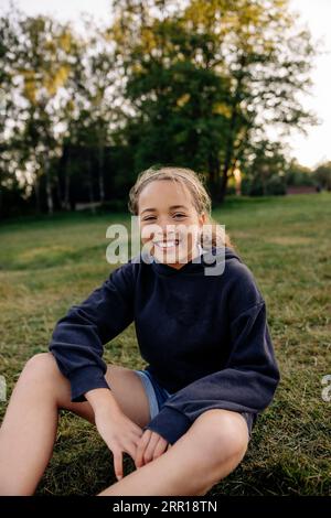 Porträt eines glücklichen Mädchens, das auf dem Rasen auf dem Spielplatz sitzt Stockfoto