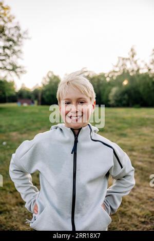 Porträt des lächelnden Jungen, der mit den Händen in den Taschen auf dem Spielplatz steht Stockfoto