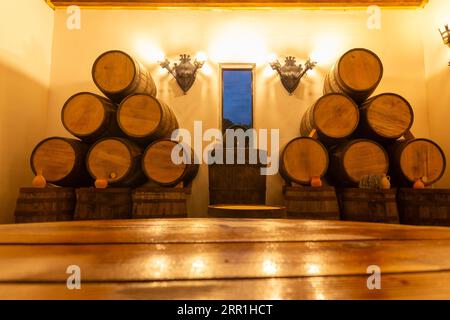 Das Weinrestaurant mit rustikalem Holztisch und Eichenfässern im Hintergrund ist im Innenraum eingerichtet. Kopierbereich für Ihr Produkt. Tonkrüge für Getränke. Stockfoto