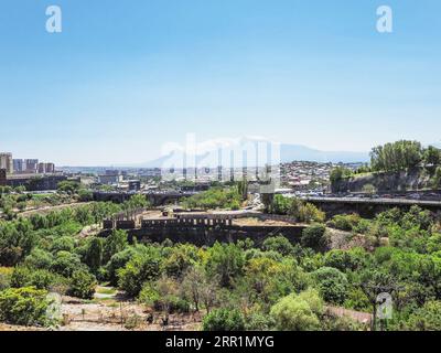 Jerewan, Armenien - 26. August 2023: Blick auf die Hrazdan-Schlucht mit der Brandy-Fabrik in Jerewan und den Ararat-Berg von der Sergey Parajanov-Straße auf der Sonne Stockfoto