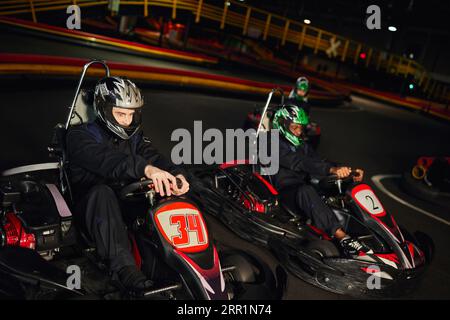 Konzentrierte multikulturelle Rennfahrer, die Go-Kart-Wagen auf Indoor-Strecken, Speedrennen und Motorsport fahren Stockfoto