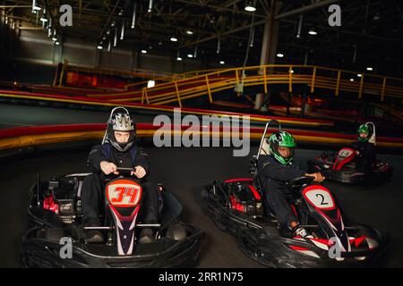 Konzentrierte multikulturelle Go-Kart-Rennfahrer, die auf Indoor-Strecken, Speedrennen und Motorsport fahren Stockfoto