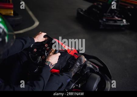 Rennfahrer im Helm und Sportbekleidung fahren Go-Kart auf Indoor-Rundkurs, Lenkrad, Adrenalin-Konzept Stockfoto