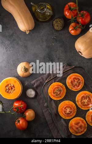 Draufsicht auf Reifen ganzen und geschnittenen Butternusskürbis und geschnittenen Tomaten, die auf einer glatten Oberfläche und auf einem Glastablett in der Küche zu Hause platziert werden Stockfoto