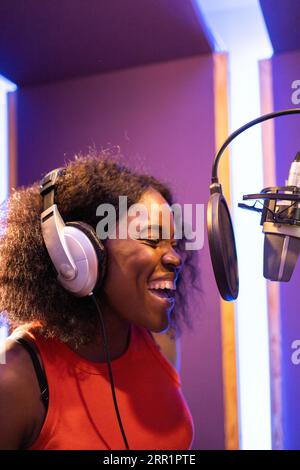 Seitenansicht einer afroamerikanischen professionellen Sängerin in Kopfhörern, die beim Singen und Aufnehmen in musikalischen Studien in der Nähe des Mikrofons hohe Noten macht Stockfoto