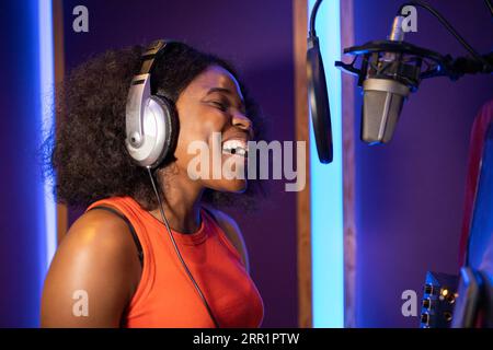 Seitenansicht einer afroamerikanischen professionellen Sängerin in Kopfhörern, die beim Singen und Aufnehmen in musikalischen Studien in der Nähe des Mikrofons hohe Noten macht Stockfoto