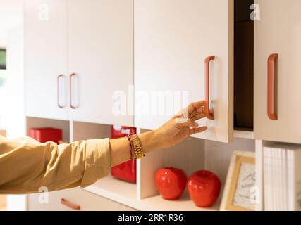 Eine anonyme Frau, die bei Tageslicht im Möbelgeschäft Küchenschränke aus Holz mit Utensilien und Dummy-Früchten zeigt Stockfoto