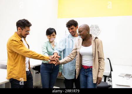 Gruppe von lächelnden Teammitgliedern, die nach unten schauen, während sie im Büro zusammenstehen und die Hände in Einheit und Übereinstimmung während der Projektarbeit stapeln Stockfoto