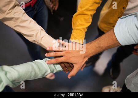 Von oben anonyme Teammitglieder in lässiger Kleidung, während sie im Kreis zusammenstehen und die Hände in Einheit gegen unscharfen Boden stapeln Stockfoto