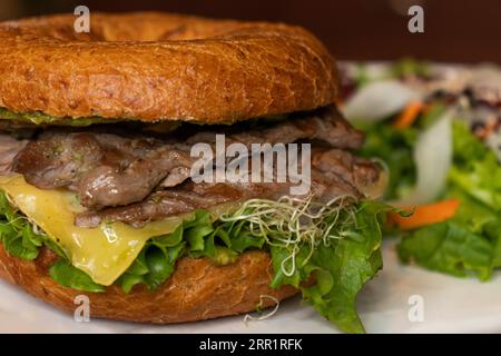 Nahaufnahme eines leckeren Burgers mit Vollkornkäse frischem Salat und Gemüse Karottensprossen auf dem Teller vor verschwommenem Hintergrund in der Küche Stockfoto