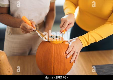 Hohe Winkel der Ernte anonyme weibliche Freunde, die am Tisch stehen und die Spitze des orangefarbenen Kürbis bei Tageslicht schneiden Stockfoto