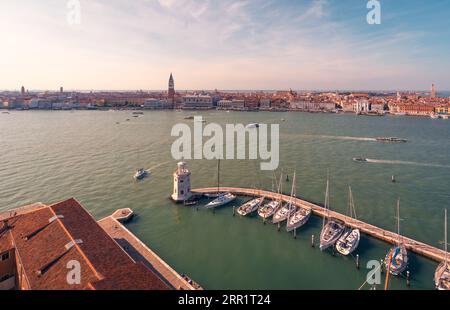 Malerischer Blick aus der Vogelperspektive auf die Stadt mit Booten, die auf dem Kanal segeln, und dem historischen St. Marks Campanile und roten überdachten Gebäuden vor dem bewölkten Sonnenuntergang Stockfoto