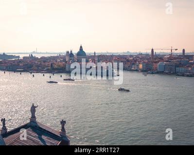 Malerischer Blick aus der Vogelperspektive auf die Stadt mit Booten, die auf dem Kanal segeln, und dem historischen St. Marks Campanile und roten überdachten Gebäuden vor dem bewölkten Sonnenuntergang Stockfoto