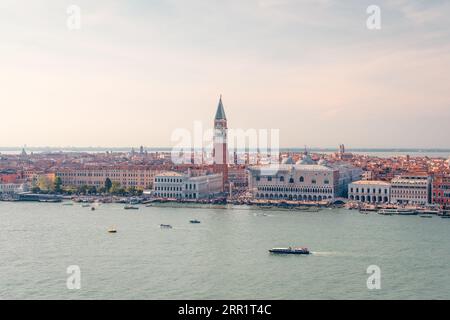 Traditionelles Vaporetto und Motorboote, die auf einem plätschernden Kanal in der Nähe der malerischen historischen Markusdom mit hohem Glockenturm gegen den Sonnenuntergang in Veni schweben Stockfoto