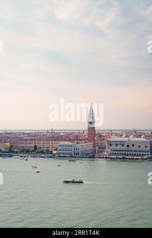 Traditionelles Vaporetto und Motorboote, die auf einem plätschernden Kanal in der Nähe der malerischen historischen Markusdom mit hohem Glockenturm gegen den Sonnenuntergang in Veni schweben Stockfoto