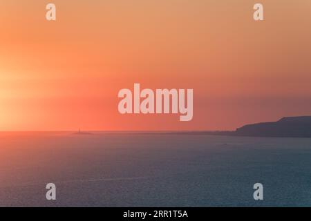 Atemberaubender Blick auf das Leuchtfeuer im Hintergrund der orangen Sonne im Sonnenuntergang über dem Meer in Marokko Stockfoto