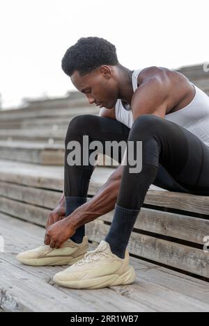 Ein ganzer Körper aus afroamerikanischen Sportlern, die auf hölzernen Treppen sitzen und Schnürsenkel an Sneakers binden Stockfoto