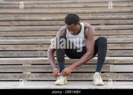 Ein ganzer Körper aus afroamerikanischen Sportlern, die auf hölzernen Treppen sitzen und Schnürsenkel an Sneakers binden Stockfoto