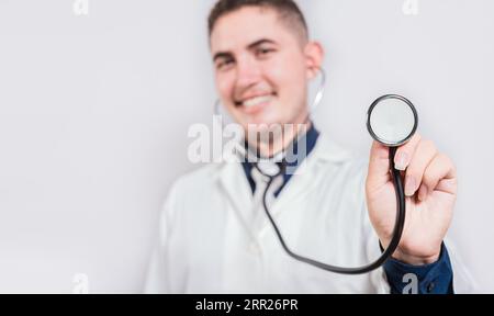Glücklicher junger Arzt, der ein Stethoskop hält, das auf die Kamera schaut. Porträt eines lateinischen Arztes, der das Stethoskop isoliert hält Stockfoto